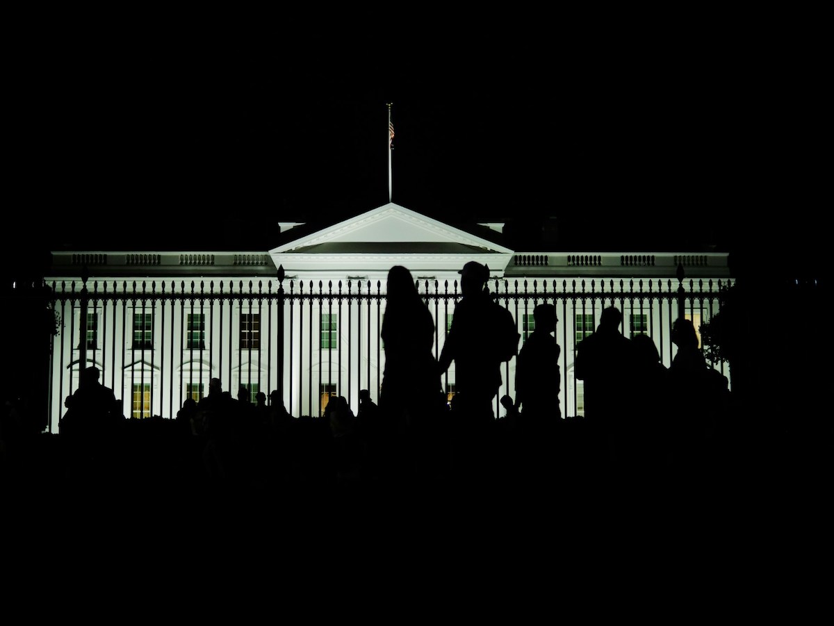 Image of The White House in Washington DC at night, with a crowd looking at it.